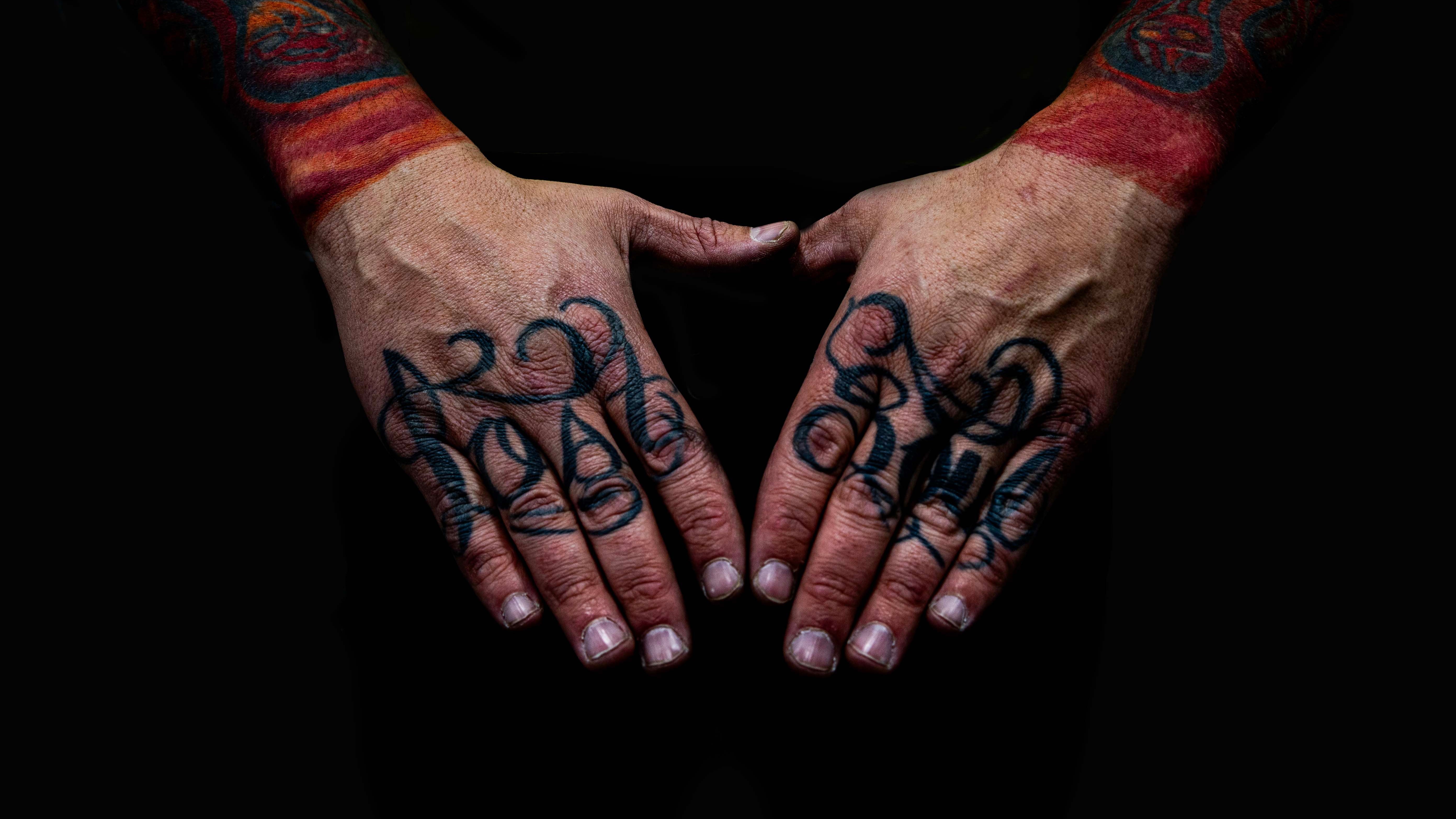 Duas mãos com lettering em blackwork nos dedos e punhos